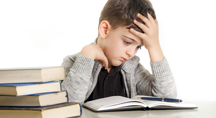 Young boy leaning over a book, looking discouraged